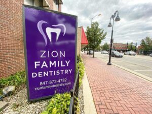 Letrero de Zion Family Dentistry frente al edificio que se encuentra en una calle de la ciudad con coches